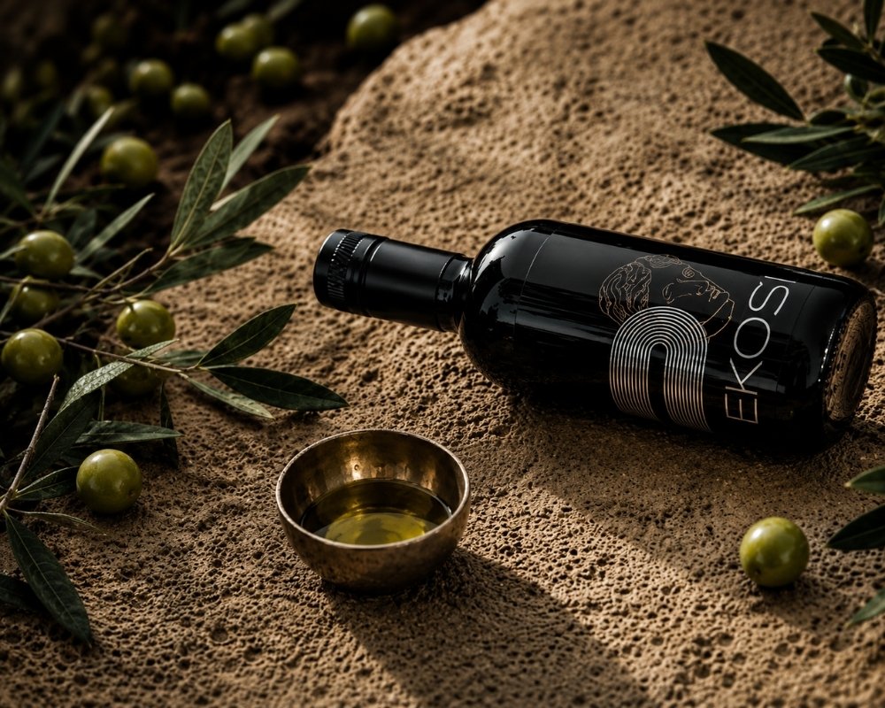 EKOSI Extra Vergine Olivenöl auf Naturstein mit frischen grünen Oliven, Olivenzweigen und einer Schale Olivenöl. Mediterrane Produktinszenierung des nativen Olivenöls extra aus Kreta in hochwertigem Ambiente.
