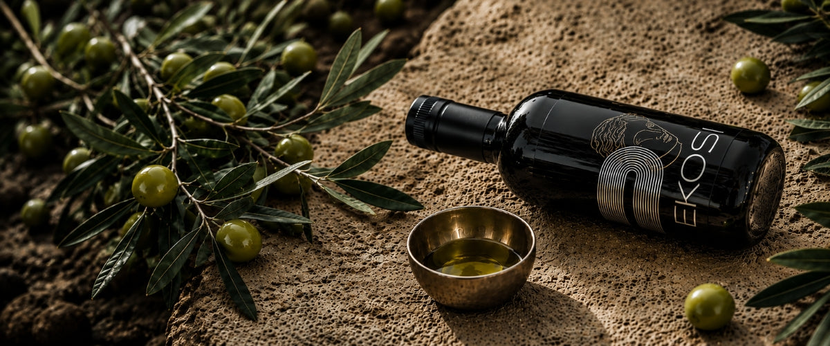 EKOSI Extra Natives Olivenöl auf einer Natursteinplatte mit frischen grünen Oliven, Olivenzweigen und einer Schale mit goldenem Olivenöl. Stilvolle mediterrane Produktinszenierung mit Fokus auf hochwertige Zutaten und authentischen Genuss.