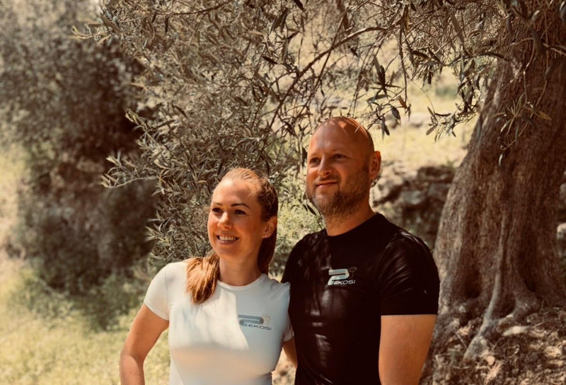 Die Gründer von EKOSI stehen unter einem jahrhundertealten Olivenbaum auf Kreta. Das Bild zeigt den Ursprung der Marke und die enge Verbindung zu traditionellem Olivenanbau, regionaler Qualität und echter Handwerkskunst.